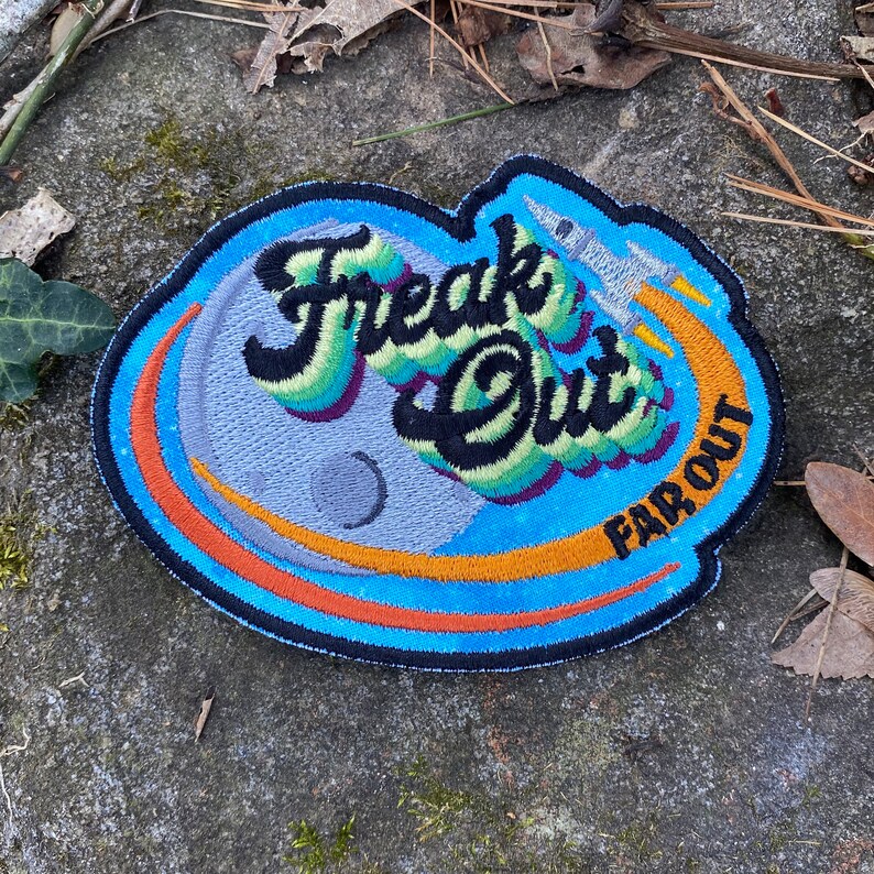 May include: Embroidered patch with the words "Freak Out" in a colorful, stylized font, with "Far Out" below. The design includes a rocket ship and a planet, set against a blue and orange background.