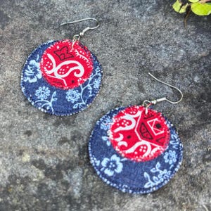May include: A pair of handmade fabric earrings. Each earring features a red paisley center, surrounded by a navy blue floral patterned fabric. The earrings have silver-colored ear wires.