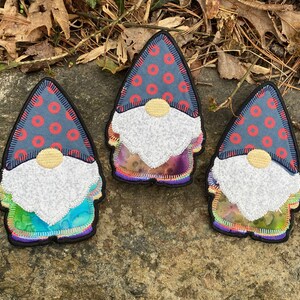 May include: Three gnome-shaped patches with a whimsical design. Each patch features a blue hat with red circles, a white beard, and a colorful, tie-dye-like body. The patches are outlined in black.