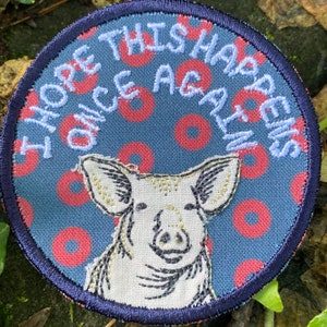May include: Round patch with a navy blue border and a blue background with red circles. The patch features a pig illustration and the embroidered text "I HOPE THIS HAPPENS ONCE AGAIN" in white thread.