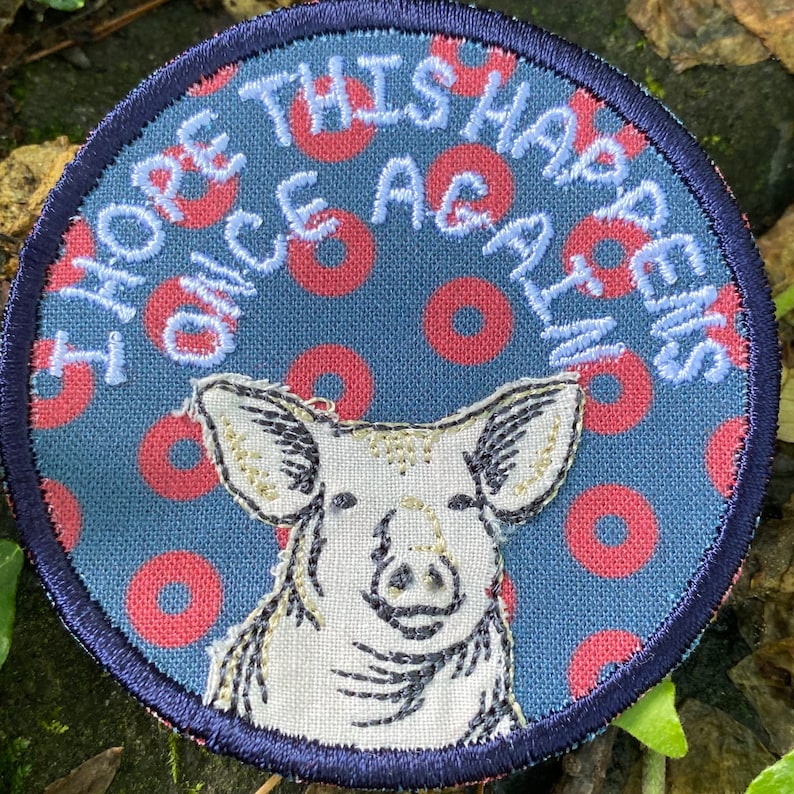 May include: Round patch with a navy blue border and a blue background with red circles. The patch features a pig illustration and the embroidered text "I HOPE THIS HAPPENS ONCE AGAIN" in white thread.