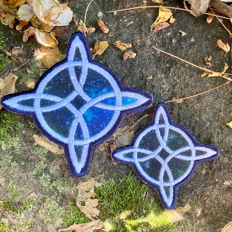 May include: Two embroidered patches featuring a Celtic knot design. The patches have a dark blue background with a starry pattern and a light blue border. One patch is larger than the other.