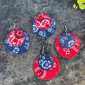 May include: Four pairs of round earrings with silver hooks. Each earring features a layered design with a red paisley pattern and a navy blue floral pattern. The earrings are set against a textured gray surface.