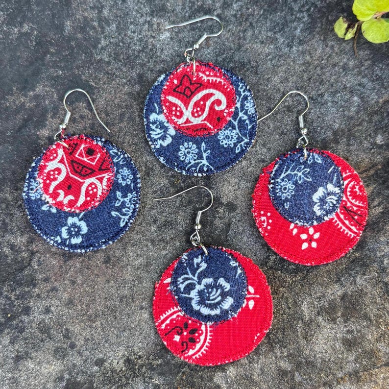 May include: Four pairs of round earrings with silver hooks. Each earring features a layered design with a red paisley pattern and a navy blue floral pattern. The earrings are set against a textured gray surface.