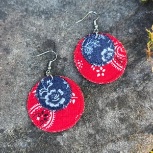 May include: Handmade fabric earrings featuring a layered design. The earrings have a red paisley pattern base with a navy blue floral center. The earrings are finished with silver-colored ear wires. A unique accessory for everyday wear.