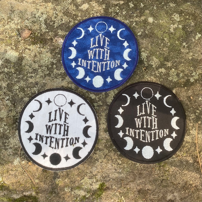 May include: Three circular embroidered patches with the text "LIVE WITH INTENTION". One is navy blue with white detailing, one is white with black detailing, and the third is black with white detailing. Each patch features crescent moons and stars.