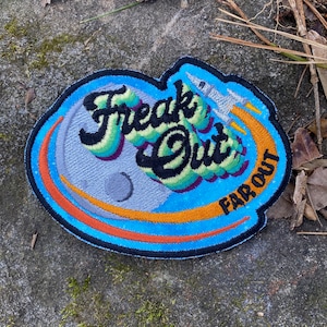 May include: Embroidered patch with the words "Freak Out" in a colorful, stylized font, with a rocket ship blasting off. The patch features a blue border, a gray moon, and the words "Far Out".