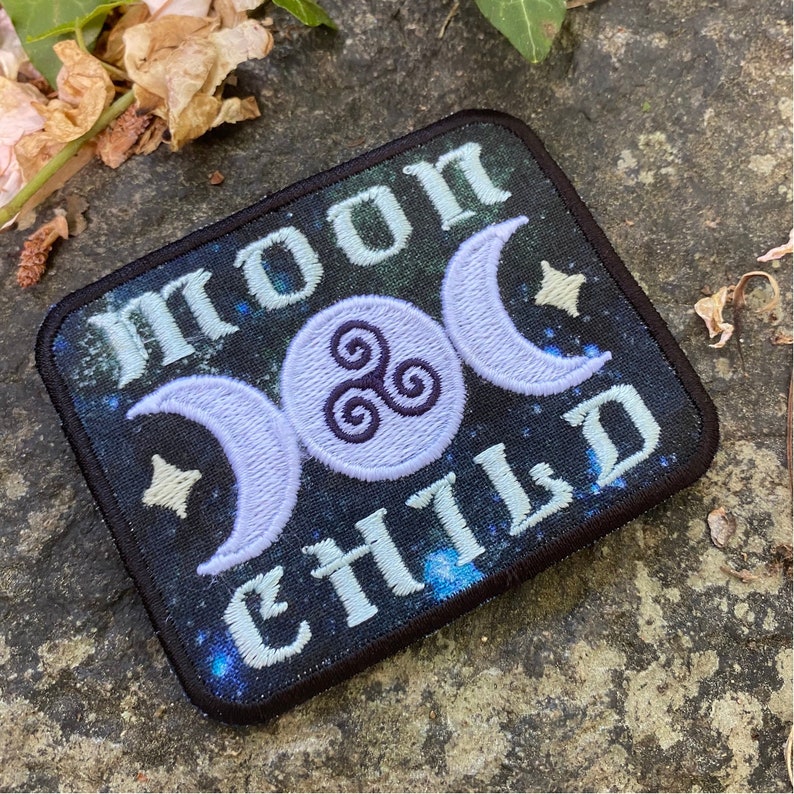 Op de afbeelding: Geborduurde patch met de woorden "MOON CHILD" in lichtblauw, met een drievoudig maansymbool en sterren op een donkerblauwe achtergrond. De patch heeft een zwarte rand.