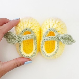 Puede incluir: Un par de zapatos de bebé de ganchillo hechos a mano. Los zapatos son amarillos con una correa verde y detalles de hojas. El interior del zapato es amarillo. Los zapatos están diseñados para parecer sandalias.