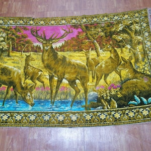 Könnte beinhalten: Rechteckige Tapisserie mit einer Waldszene mit Hirschen. Die Tapisserie hat einen gelb-grünen Rand mit einem Blumenmuster. Das zentrale Bild zeigt mehrere Hirsche in der Nähe eines Gewässers, mit einem rosa und gelben Himmel im Hintergrund.