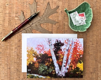 May include: An autumn-themed still life featuring a landscape painting of birch trees with vibrant fall foliage. A burgundy fountain pen, a green leaf-shaped dish with stamps, and a dried leaf complete the composition.