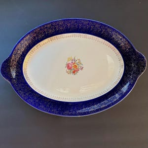 May include: Oval serving platter with a white center and a blue rim with gold filigree. The center features a floral bouquet. The platter is approximately 16 inches long and 10 inches wide.
