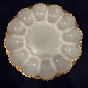 May include: A white, scalloped-edge serving dish with a gold-colored rim. The dish has a central circular area surrounded by twelve petal-shaped compartments. The gold rim adds a touch of elegance to this decorative piece.