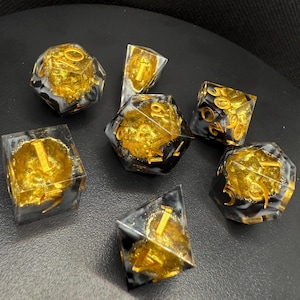 May include: A set of seven polyhedral dice. Each die is clear with a gold-coloured interior and black and white marbling. The numbers are in gold. The dice are for role-playing games.