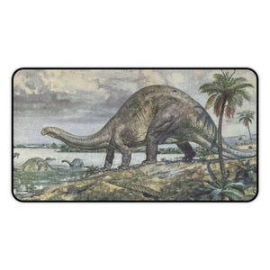 May include: A rectangular wall art print featuring a prehistoric scene with a large, long-necked sauropod dinosaur standing on a grassy bank. In the background, a body of water contains smaller dinosaurs, and a palm tree stands on the right side.