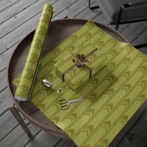 May include: A roll of olive green wrapping paper featuring a repeating pattern of dark green chevron arrows, a rectangular gift box wrapped in the same paper with a brown ribbon bow, a small roll of clear tape, and silver metal scissors.