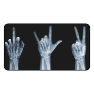 May include: A black rectangular mousepad featuring an x-ray image of three hands. The hands display the middle finger, the 'I love you' hand gesture, and the peace sign. The image is in shades of gray and white.