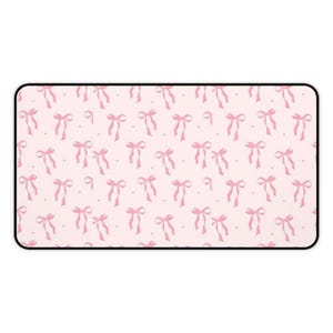 Puede incluir: Alfombrilla de ratón rectangular rosa con un patrón repetido de lazos rosas y pequeños puntos. La alfombrilla tiene un borde negro. Los lazos están atados en el centro y tienen cintas largas y fluidas. El fondo es de color rosa claro.