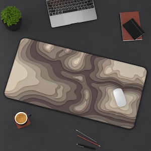 May include: A rectangular desk mat featuring a layered topographic map design in shades of brown, tan, and cream. The surface displays smooth, flowing contour lines that create a depth effect across the entire mat, providing a workspace area.