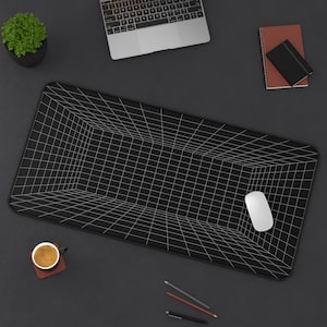 Pode incluir: Tapete de mesa preto com um design de grade branca, um mouse de computador branco e uma pequena planta em vaso. Um laptop, um caderno e lápis também estão na superfície escura. O tapete tem um design de perspectiva 3D.