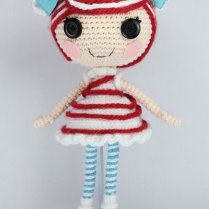 May include: A crocheted doll with red and white striped clothing, blue and white striped leggings, and red shoes. The doll has a red and white striped hat with a blue bow. The doll has large black eyes and a smiling face.