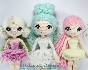 May include: Three crocheted dolls with different colored hair and dresses. The doll on the left has blonde hair and a pink dress, the middle doll has teal hair and a white dress, and the doll on the right has pink hair and a yellow dress. All three dolls have wings and are smiling.