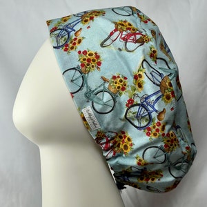 May include: A blue and white patterned scrub hat with a design of bicycles and sunflowers. The hat has a white label with the text "Bullyboy & Sailor".