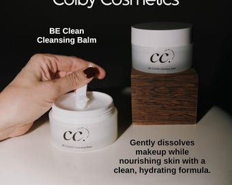 May include: White Colby Cosmetics cleansing balm jars. One jar is open with a white applicator. The text "BE Clean Cleansing Balm" is visible. The text "Gently dissolves makeup while nourishing skin with a clean, hydrating formula" is also visible.