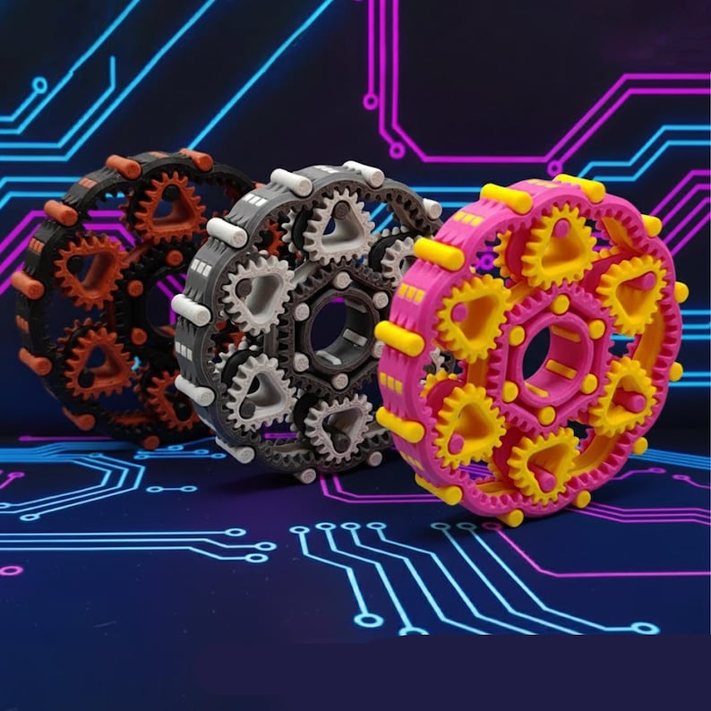 May include: Three colorful gear-shaped objects. One is black with orange gears, another is gray with white gears, and the third is pink with yellow gears. The gears are arranged in a circular pattern, with a central hole.