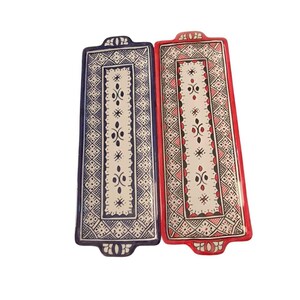 May include: Two rectangular ceramic serving trays. One is navy blue with a white and black geometric pattern. The other is red with a white and black geometric pattern. Both have decorative handles.