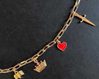 May include: Gold-toned necklace with a chain link design. The necklace features charms including a star, dagger, red heart, crown, and an open book. The charms are suspended from the chain, creating a decorative and eye-catching accessory.