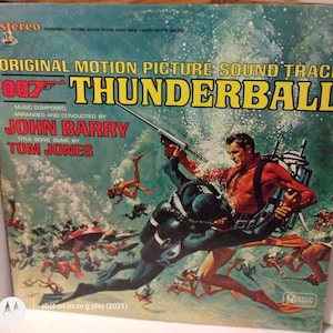 May include: Vintage vinyl record album cover for the James Bond film "Thunderball." The cover features a dynamic illustration of divers in a turquoise underwater scene, with the title and credits in bold yellow and red text. The album is a stereo recording.