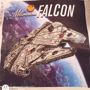 May include: A diamond painting kit featuring the Millennium Falcon starship against a backdrop of space and a planet. The words "Millennium Falcon" are displayed in white, with the Star Wars logo. The ship is detailed with various shades of gray and brown.