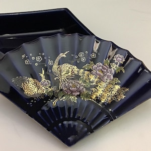 May include: A navy blue ceramic trinket box with a fan-shaped lid. The lid is decorated with gold and purple peacock and floral designs. The box is rectangular and has a glossy finish.