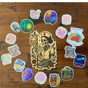 May include: A collection of colorful stickers with medical and nursing themes. Designs include a skeleton nurse, brain anatomy, and phrases like "Night Shift" and "Straight Outta Clinicals". The stickers are arranged on a wooden surface.