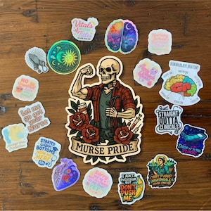 May include: A collection of colorful stickers with various designs. The stickers include a skeleton in a plaid shirt with the text "MURSE PRIDE", a brain, a crescent moon and sun, and other medical and nursing-themed graphics. The stickers are on a wooden surface.