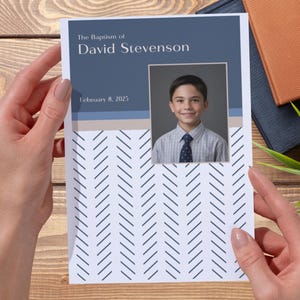 May include: A baptism announcement featuring a photo of a young boy in a collared shirt and tie. The top section is navy blue with the text "The Baptism of David Stevenson" and the date "February 8, 2025". The bottom has a white chevron pattern.