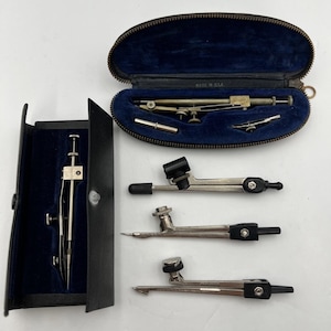 Peut inclure: Ensemble d'instruments de dessin anciens, comprenant des compas et des diviseurs, présentés dans un étui en cuir noir avec un intérieur en velours bleu. Plusieurs outils sont exposés séparément, soulignant leurs designs détaillés et finitions métalliques.