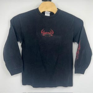 May include: Black long-sleeve shirt with red flame graphics on the sleeves and a small design on the chest. The chest design reads "Orange County" in a stylized font. The shirt is made of a soft material and has a classic crew neck.