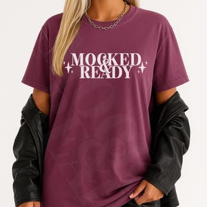 Op de afbeelding: Een bordeauxrood t-shirt met de tekst "MOCKED & READY" in het wit. Het shirt wordt gecombineerd met een zwarte short en een zwarte leren jas. Een zilveren ketting is ook zichtbaar.