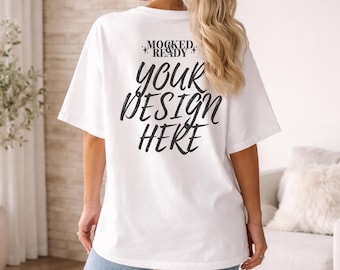 Op de afbeelding: Wit oversized T-shirt met de tekst "MOCKED READY" boven "YOUR DESIGN HERE" in een zwarte, handgeschreven lettertype. Het shirt heeft korte mouwen. Het model draagt een blauwe jeans.
