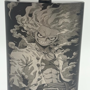 May include: A black stainless steel flask with a silver cap and hinge. The flask features a detailed etched image of a character with spiky hair and a determined expression. The design is a stylized illustration.