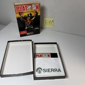 Peut inclure: Un coffret de jeu vidéo vintage Platoon pour ordinateurs Apple. La boîte verticale présente une silhouette de soldat et le titre Platoon. La boîte ouverte contient une disquette noire étiquetée Platoon et un manuel blanc avec le logo Sierra vert.