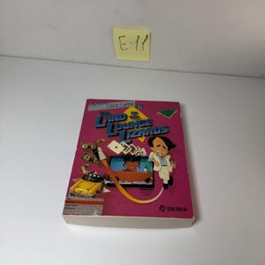 Puede incluir: Una caja rectangular de videojuego para Leisure Suit Larry in the Land of the Lounge Lizards de Sierra. La cubierta magenta presenta un personaje de dibujos animados, un taxi amarillo, cartas de juego, dinero y una pantalla.