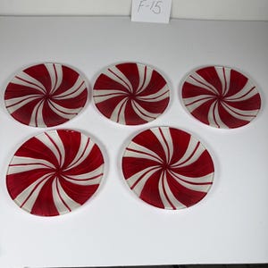 May include: Five round glass plates featuring a red and white spiral pattern radiating from the center. Each plate has a smooth surface and a translucent finish. A small white card with the handwritten text F-15 is visible at the top center.