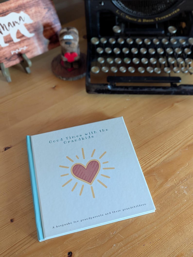 May include: A hardcover book titled "Good Times with the Grandkids" with a light blue cover and spine. The cover features a pink heart with yellow sun rays. The book is a keepsake for grandparents and their grandchildren.