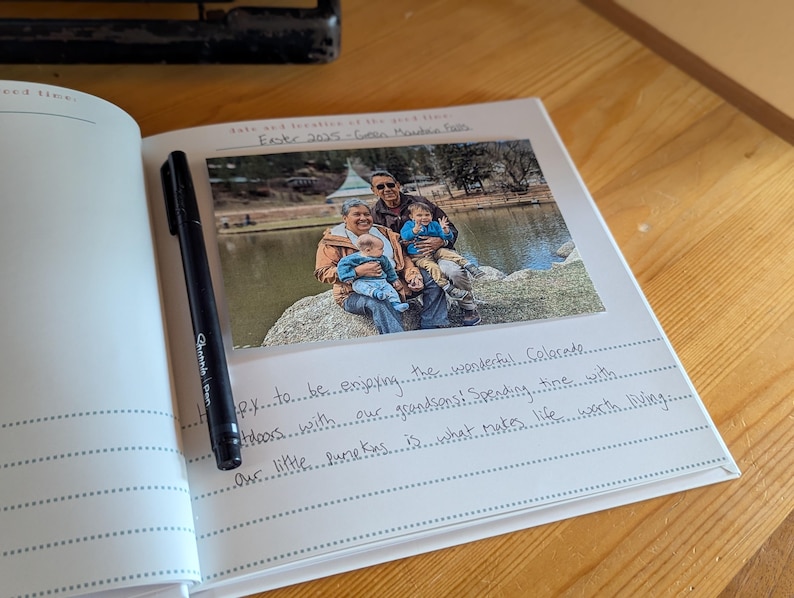 May include: An open journal with a photograph and handwritten text. A black pen rests on the left page. The photo shows a family by a lake. Text includes "Easter 2025-Green Monde" and handwritten notes about enjoying Colorado.