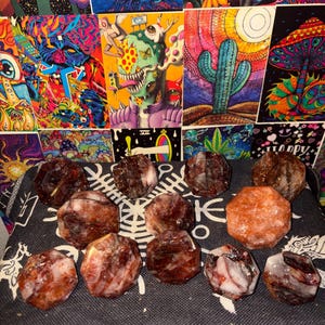 May include: A collection of twelve faceted, multi-sided stones with a polished finish. The stones exhibit a marbled appearance with deep red, brown, and translucent white color variations. Each stone features a distinct geometric shape with flat surfaces.