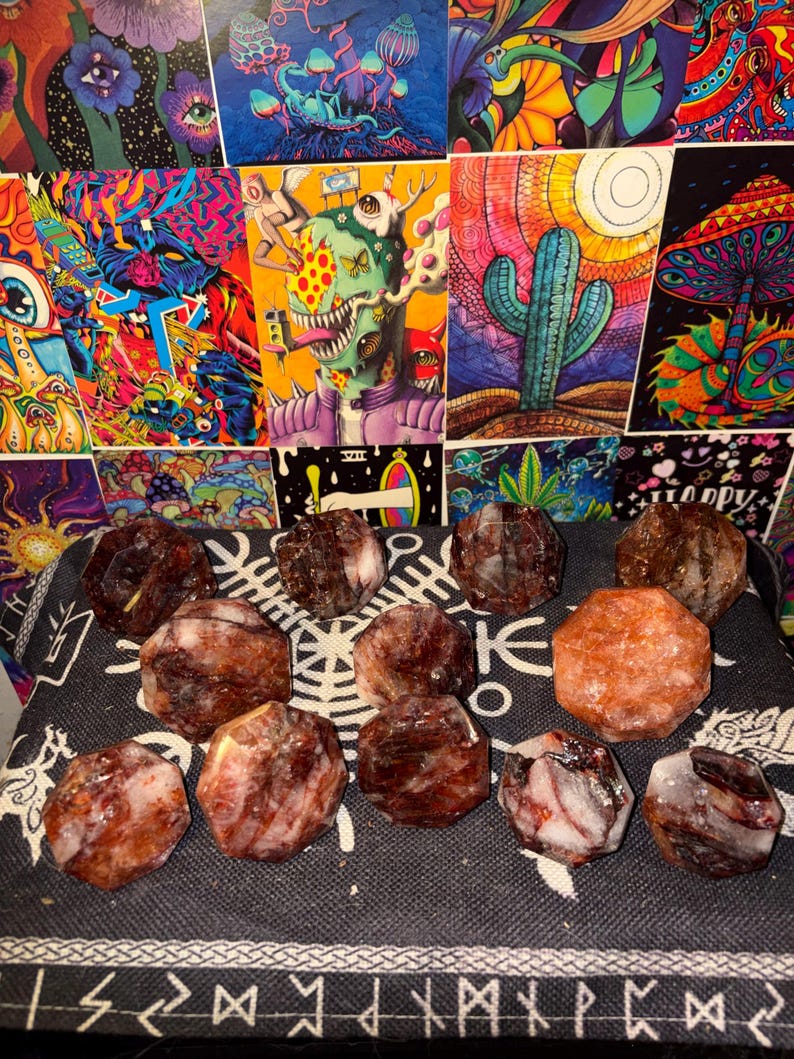 May include: A collection of twelve faceted, multi-sided stones with a polished finish. The stones exhibit a marbled appearance with deep red, brown, and translucent white color variations. Each stone features a distinct geometric shape with flat surfaces.