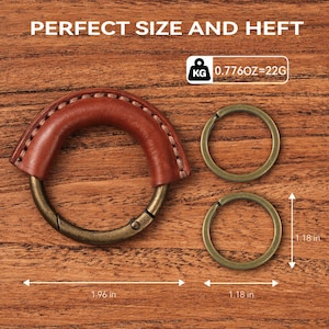 May include: A brown leather handle with a metal clasp and two metal rings. The handle is stitched with white thread. The text "PERFECT SIZE AND HEFT" is at the top. The rings are 1.18 inches in diameter. The handle is 1.96 inches long.